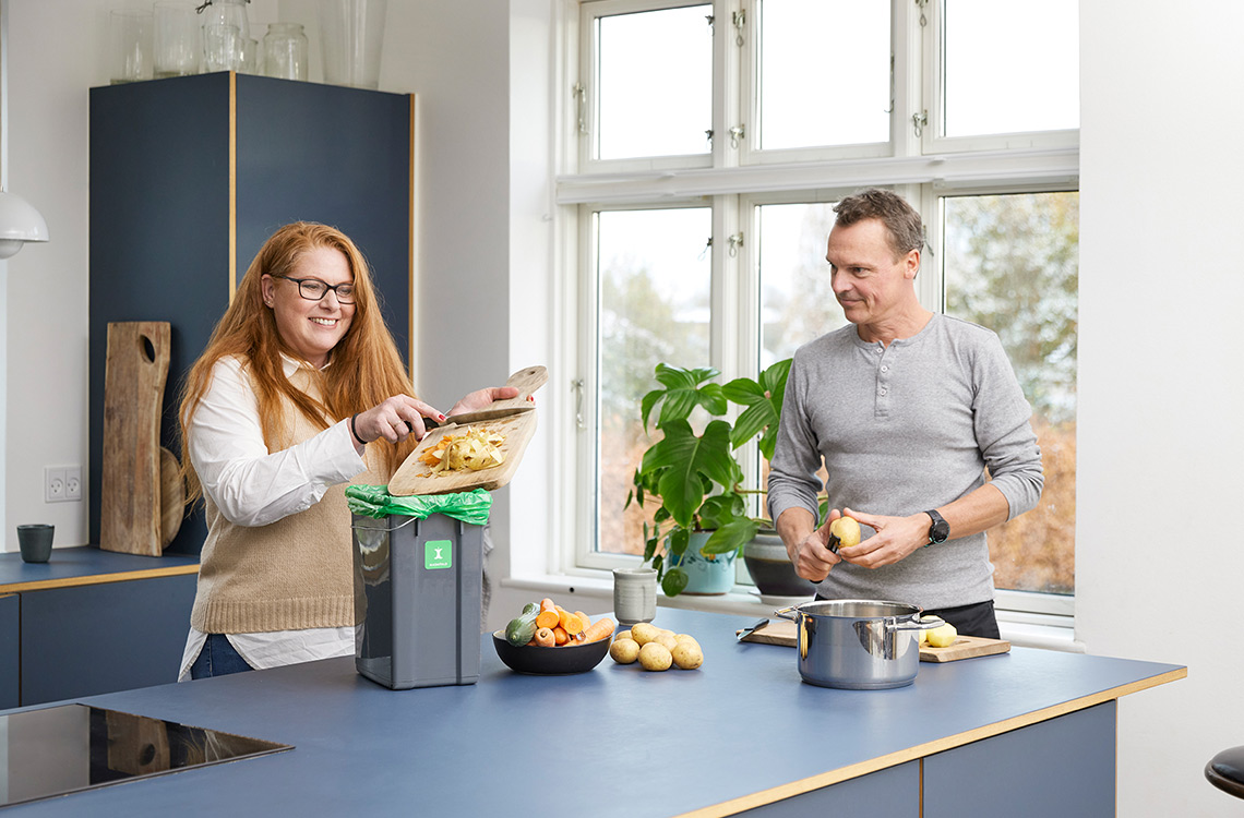 To personer sorterer madaffald på køkkenbord i villa